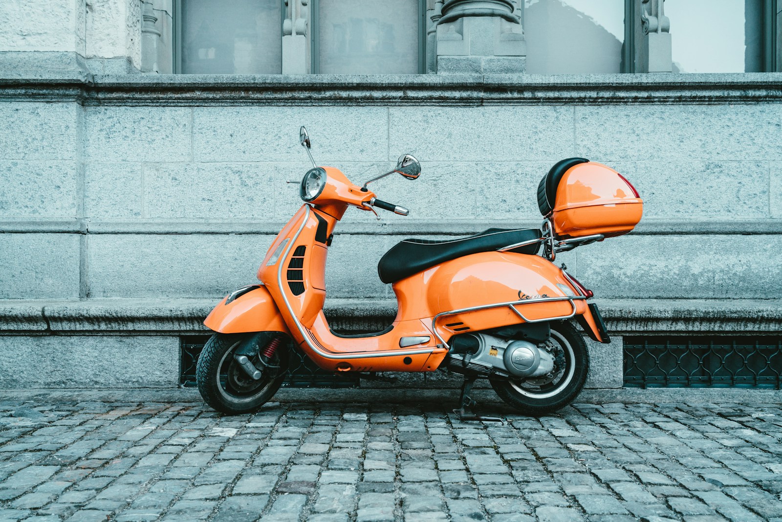 Orange motor scooter parked beside a stone wall